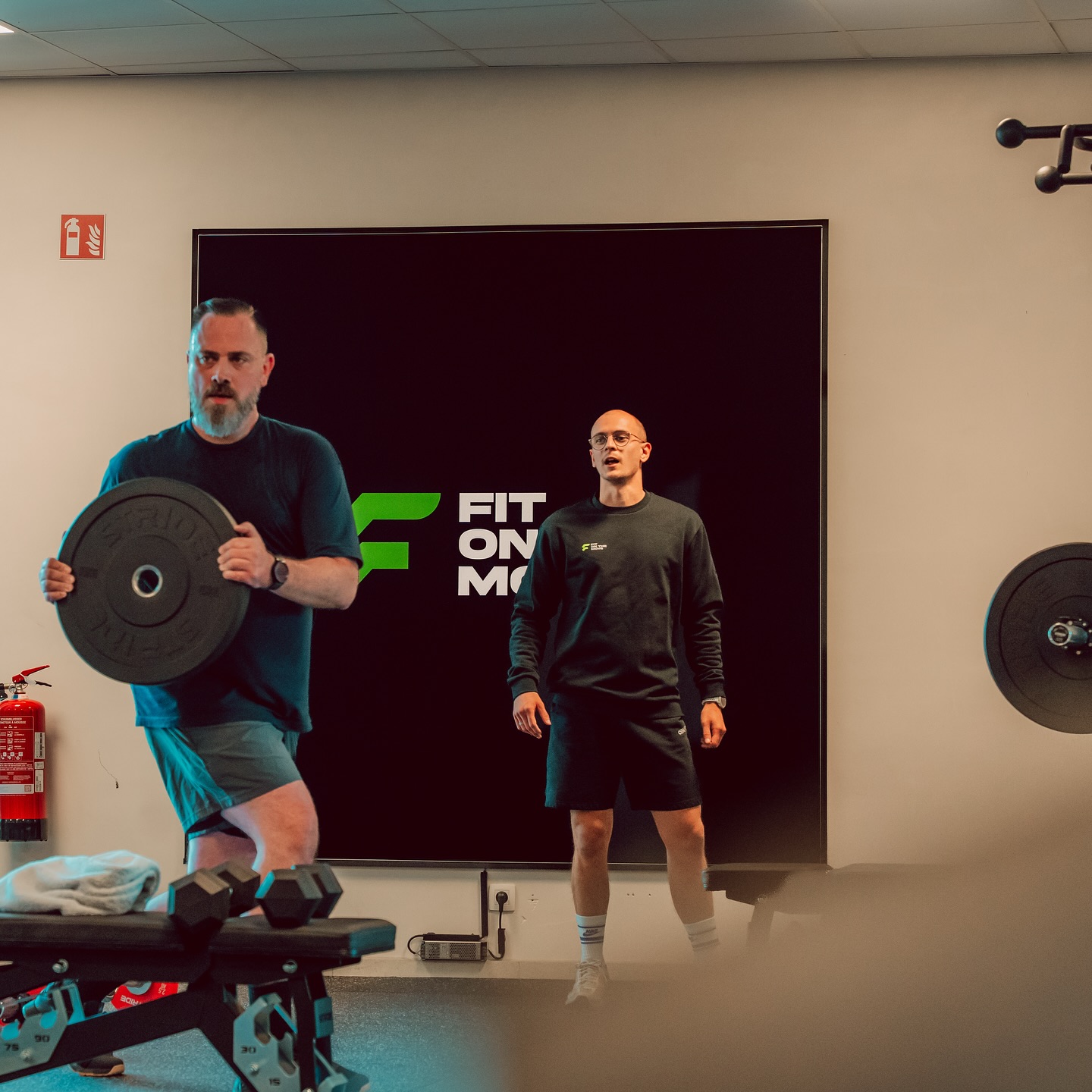 Man die traint met gewichtsschijf onder begeleiding in fitnessruimte