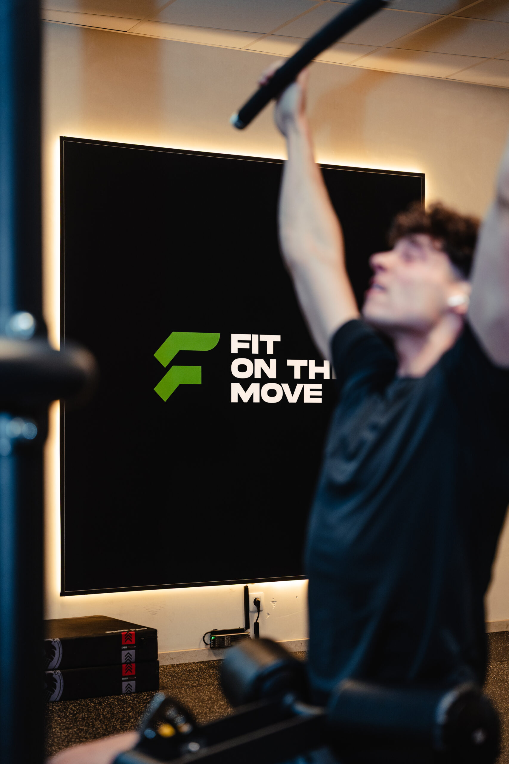 Persoon traint aan fitnessapparatuur in moderne fitnessruimte met logo Fit on The move in achtergrond