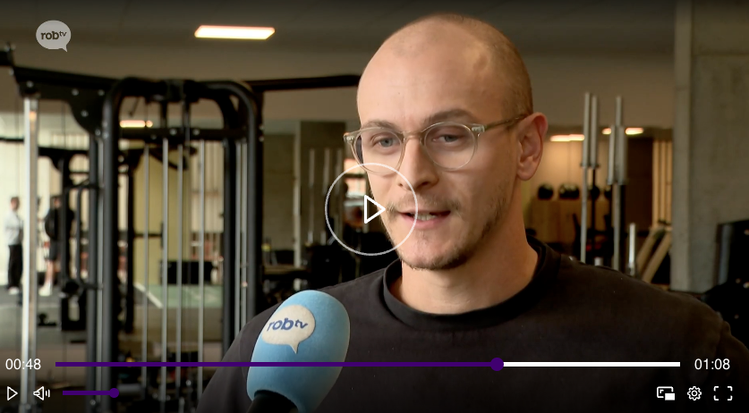 Twee mannen, Hannes Tollet en Gust Alaerts, zitten ontspannen in een moderne fitnessruimte met zitmeubilair en houten accenten tijdens de opening van hun zaak.